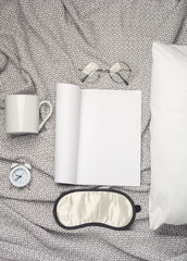 White blank magazine mockup, sleeping mask, cup, alarm clock on a blanket with pillow. Flat lay