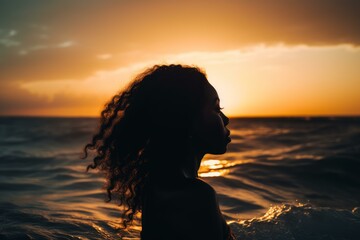 Fototapeta premium Tranquil silhouette of a curly-haired woman enjoying the sunset over the ocean waves