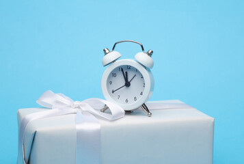 Alarm clock with gift box on a blue background. Merry Christmas