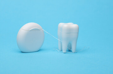 Dental floss with tooth model on blue background.