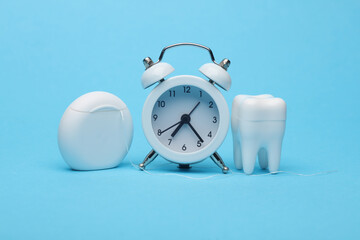 Time to take care of your oral cavity. Alarm clock with tooth model and dental floss on blue...