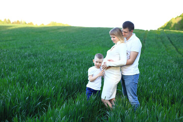 A man standing with two young boys in a field and pregnancy woman. Family expecting their third...