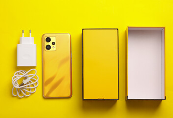 New smartphone with box and accessories on a yellow background. Yellow color trend. Modern gadgets,...