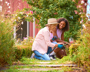 Teenage Granddaughter Helping Grandmother With Gardening At Home Learning About Plants And Nature