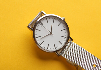 Women's wrist analog watch with metal or silver strap on yellow background