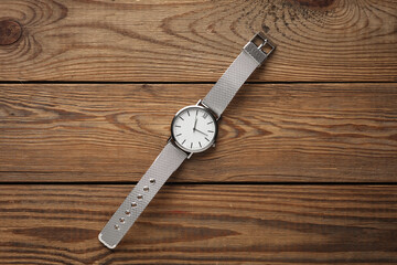 Women's wrist analog watch with metal or silver strap on wooden background.