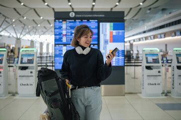 Young Asian woman in international airport looking at flight information board, checking her flight - obrazy, fototapety, plakaty