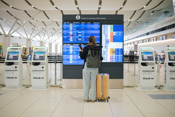 Young Asian woman in international airport looking at flight information board, checking her flight