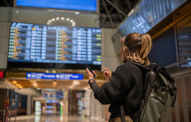 Young Asian woman in international airport looking at flight information board, checking her flight - obrazy, fototapety, plakaty