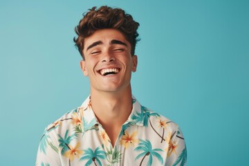 Obraz premium Portrait of a vibrant young man wearing a tropical floral shirt, laughing with eyes closed against a teal background, reflecting a carefree and joyful moment. Generated AI