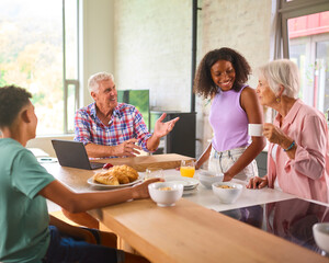 Grandparents With Teenage Grandchildren Indoors At Home Preparing And Eating Breakfast Together