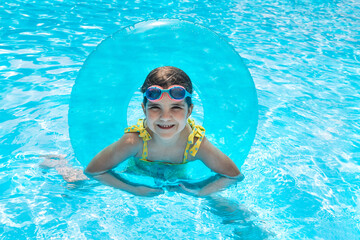 A little girl with an inflatable circle jumped into the pool. A cute kid in a swimsuit