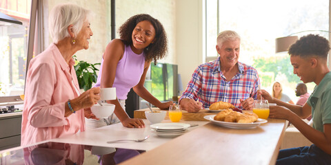 Grandparents With Teenage Grandchildren Indoors At Home Eating Breakfast With Parents In Background