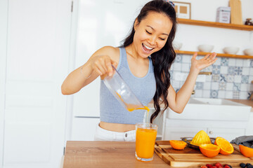Attractive smiling Asian woman makes fresh tasty healthy orange juice in the kitchen