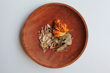 Wedang Uwuh, or Javanese herbal drink, isolated on white background. Ingredients before brewed of Indian redwood, dried ginger, lemongrass and cardamom. On wooden plate