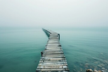 Obraz premium A weathered wooden pier extending into turquoise waters, disappearing into the hazy sunset
