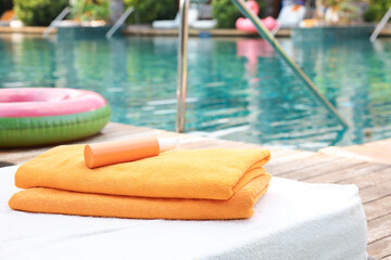 Beach towels and sunscreen on sun lounger near outdoor swimming pool, selective focus. Luxury resort