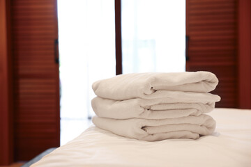 Stacked towels on bed in hotel room, space for text