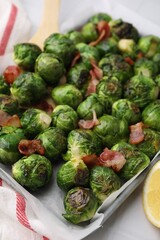 Delicious roasted Brussels sprouts and bacon in baking dish on table, closeup