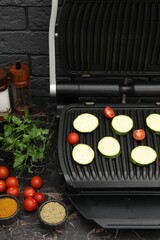 Electric grill with vegetables and spices on black marble table