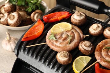 Electric grill with homemade sausages, mushrooms and bell pepper on table, closeup