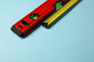 Building level and tape measure on light blue background. Space for text