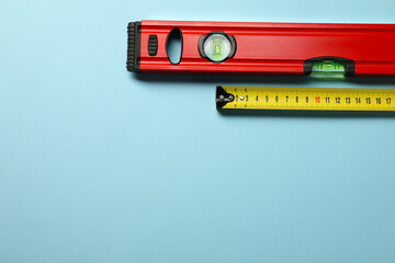Building level and tape measure on light blue background, top view. Space for text