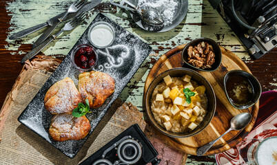 Delicious breakfast, oatmeal porridge with pieces of fruit, pastry buns with cottage cheese, on rustic background. Top view