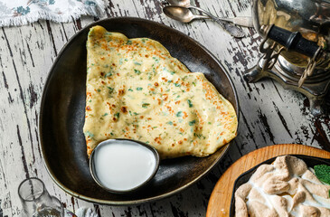 Crepes with greens, cheese and sour cream on plate on rustic background. Delicious pastry, top view