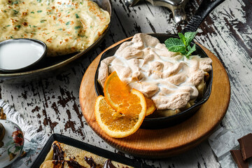 Meringue with slices of orange and mint on pan on rustic background. Sweets, dessert and pastry,...