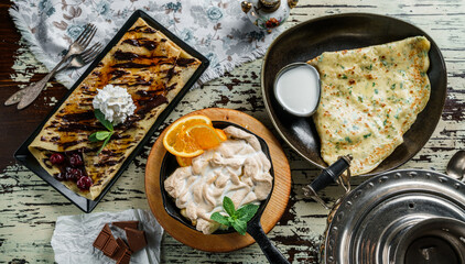 Assorted crepes or pancakes with greens, cheese, cherries, chocolate and meringue on rustic...