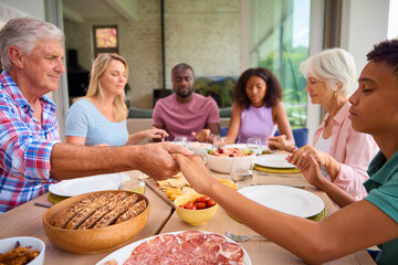 Three Generation Family Indoors At Home Saying Prayer Before Eating Meal Together