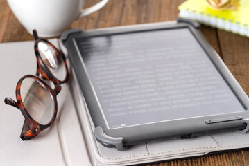 E-book, notepad on wooden table with cup of coffee and reading glasses