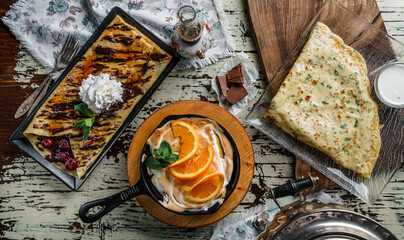 Assorted crepes or pancakes with greens, cheese, cherries, chocolate and meringue on rustic background. Healthy breakfast and lunch, top view