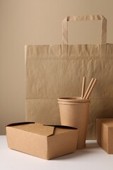 Eco friendly food packaging. Paper containers, bag and straws on white table against beige background