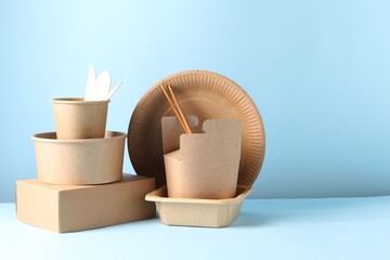 Eco friendly food packaging. Paper containers and tableware on white table against light blue background, space for text