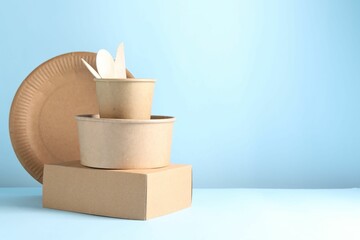 Eco friendly food packaging. Paper containers and tableware on white table against light blue background, space for text