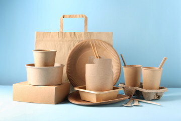 Eco friendly food packaging. Paper containers, tableware and bag on white table against light blue background