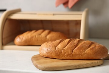 Wooden bread basket with freshly baked loaves on white marble table in kitchen