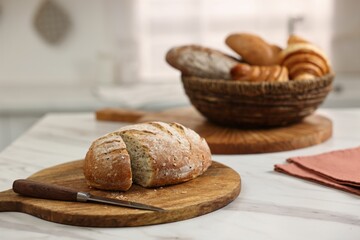 Wicker bread basket with freshly baked loaves and knife on white marble table in kitchen