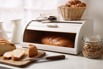 Wooden bread basket with freshly baked loaves on white marble table in kitchen