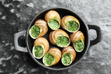 Delicious cooked snails in baking dish on grey textured table, top view