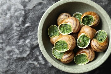 Delicious cooked snails in bowl on grey textured table, top view. Space for text