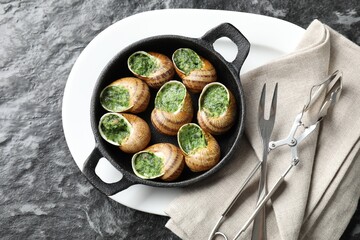 Delicious cooked snails in baking dish served on grey textured table, flat lay