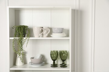 Different clean dishware and houseplant on shelves in cabinet indoors