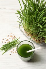 Wheat grass drink in glass, seeds and fresh green sprouts on white wooden table, flat lay