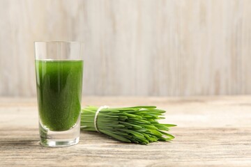 Wheat grass drink in shot glass and fresh green sprouts on wooden table, closeup. Space for text