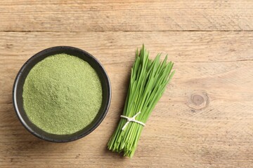 Wheat grass powder in bowl and fresh green sprouts on wooden table, flat lay. Space for text