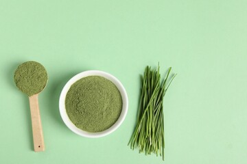 Wheat grass powder and fresh sprouts on green table, flat lay