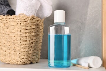 Bottle of mouthwash, toothpaste, toothbrush and towels on shelf in bathroom